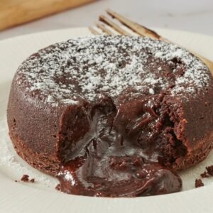 لافا كيك الشوكولاتة بقلب سائل يتدفق على طبق تقديم أبيض مع آيس كريم فانيليا